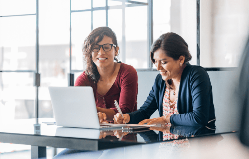 Two smiling solicitors sit together at a desk talking