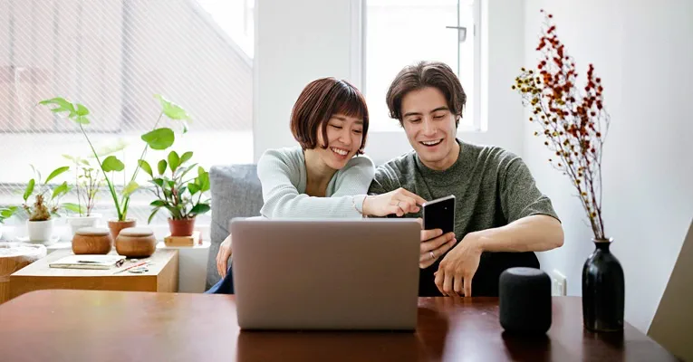 A young, mixed-race couple sit at a table looking at a mobile phone.