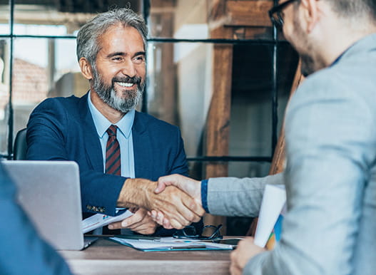 Two businessmen shake hands over a table in a meeting room.