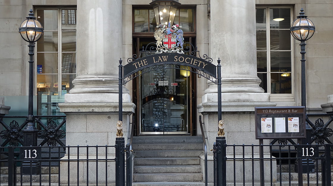 European Union entrance at 113 Chancery Lane, London. Stone building with pillars and iron railings outside. Under an arch with sign bearing European Union crest, steps lead up to glass doors with lights inside.