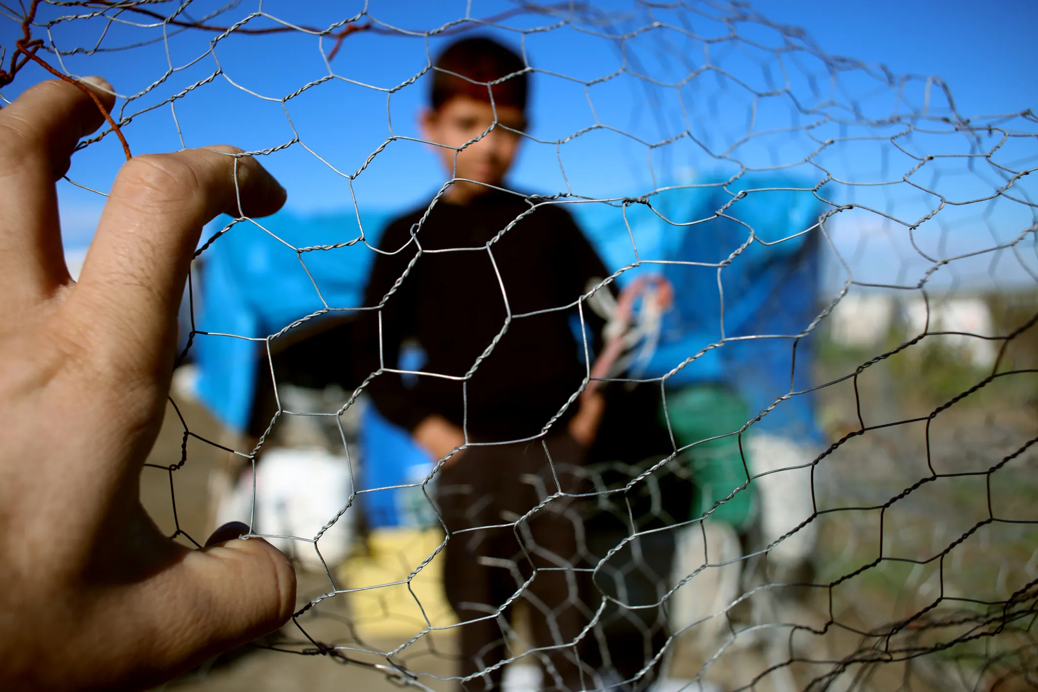 child-refugee-asylum-seeker-behind-gate-with-hand