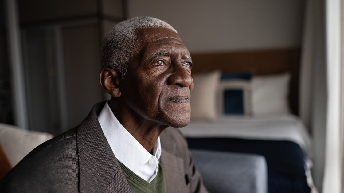 An elderly black man looks out of a window in a nursing home.