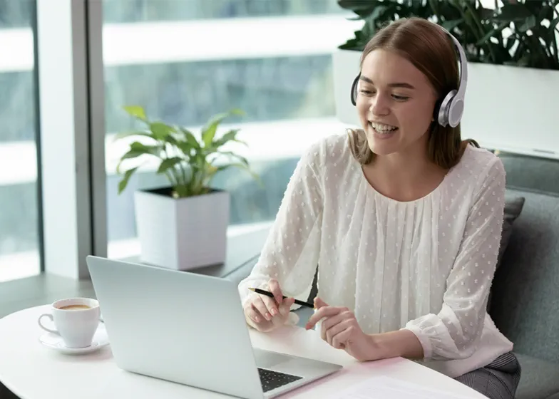 Woman with headphones on looking at computer on desk