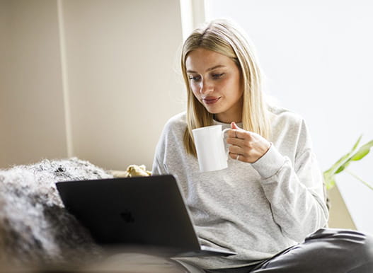 Young person holding mug whilst looking at laptop