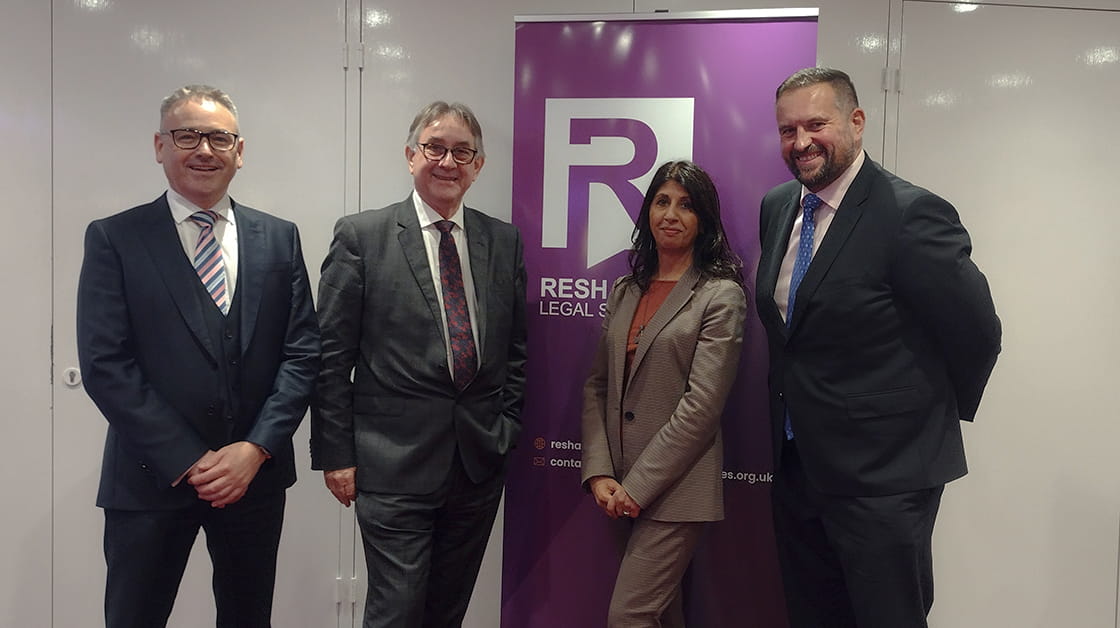 Lubna Shuja (centre right) stands with Mark Davies, Mick Antoniw MS and Gareth Jones in front of a purple Reshaping Legal Services banner.