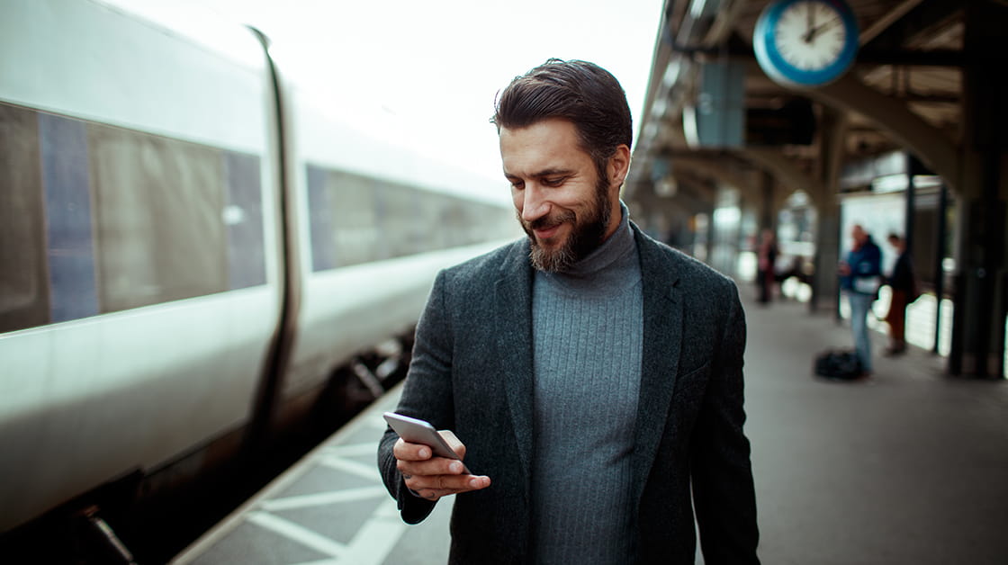 Man standing on platform scrolling mobile phone and smiling