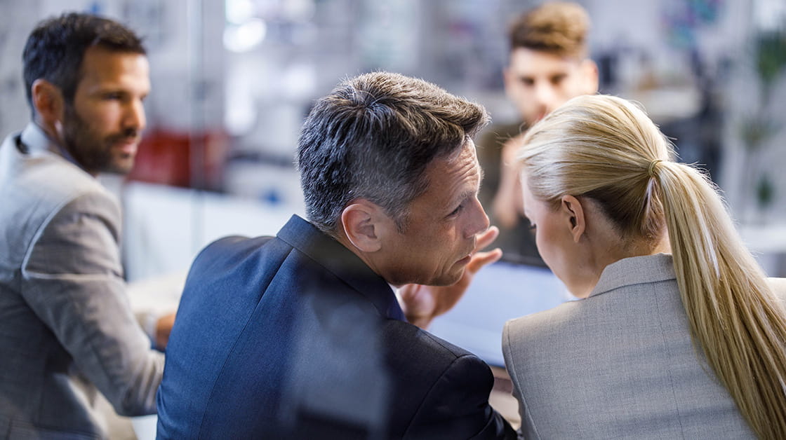 A man whispers in the ear of a woman at a meeting room board table.