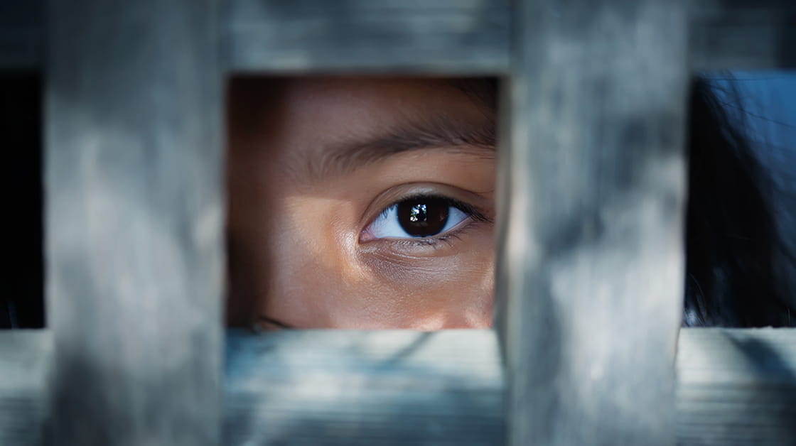 A close-up shot of a child's eye, peering out from behind a wooden frame.