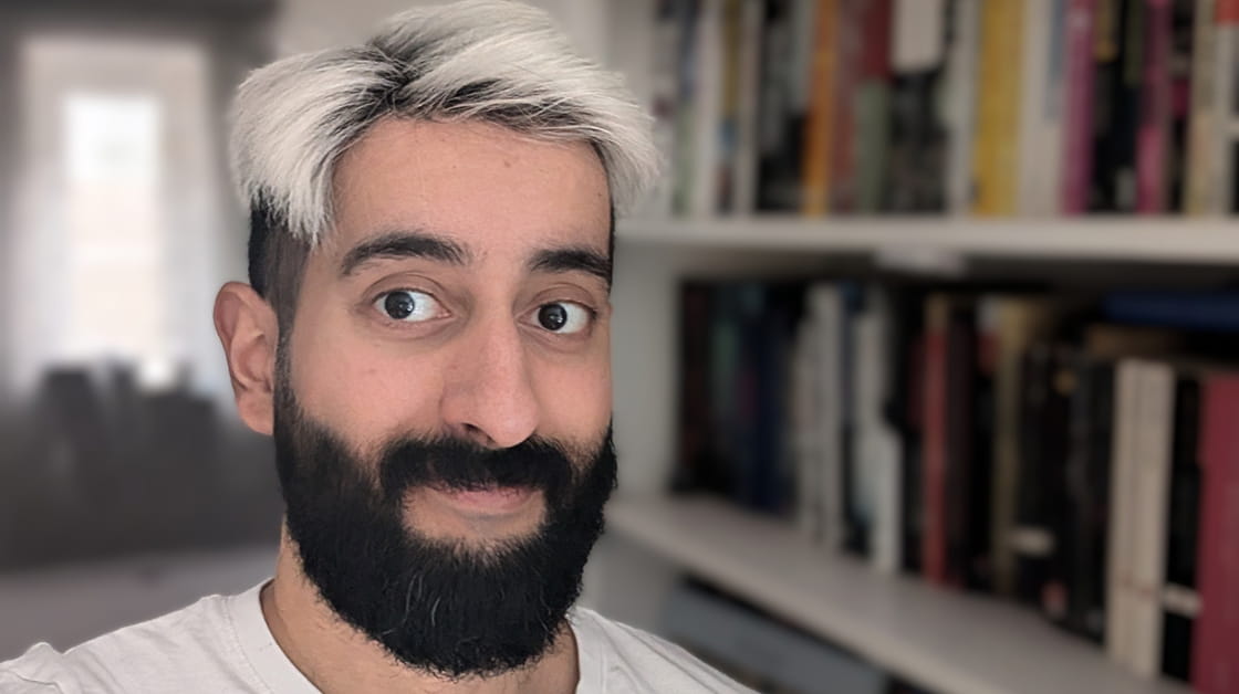 Obaid Bin Nasir is a man with short spiky silver hair and a black beard. He is smiling and stands in front of a bookshelf.