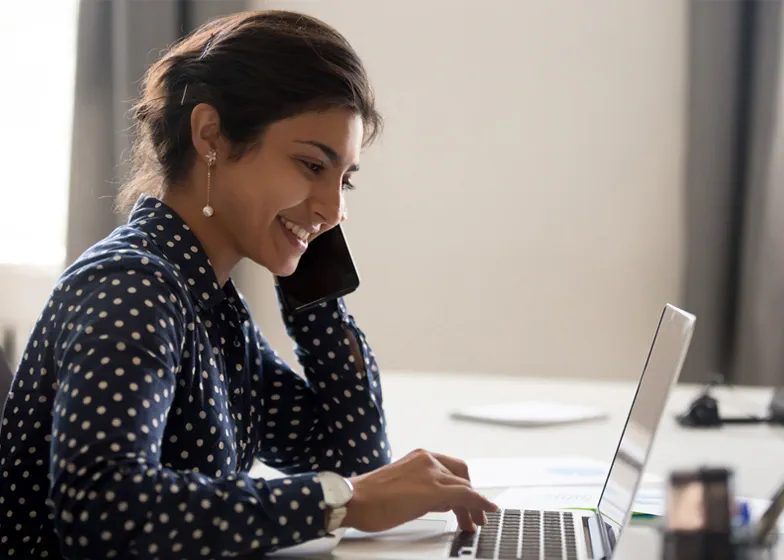 Woman working on laptop with a phone in her hand