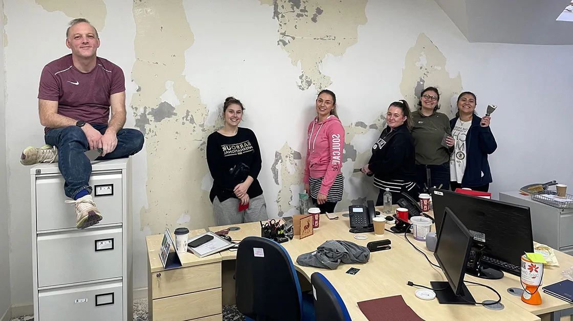 A group of people are standing in an office with painting tools, smiling at the camera. 