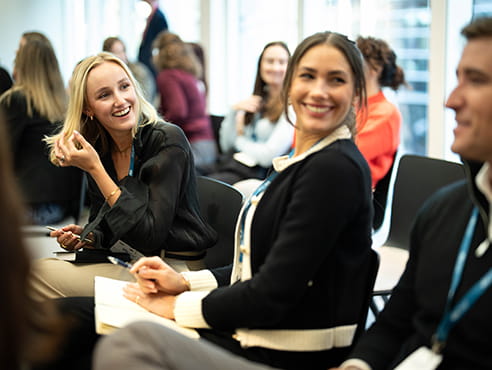 Two white woman, one blonde and one brunette are sitting down and smiling