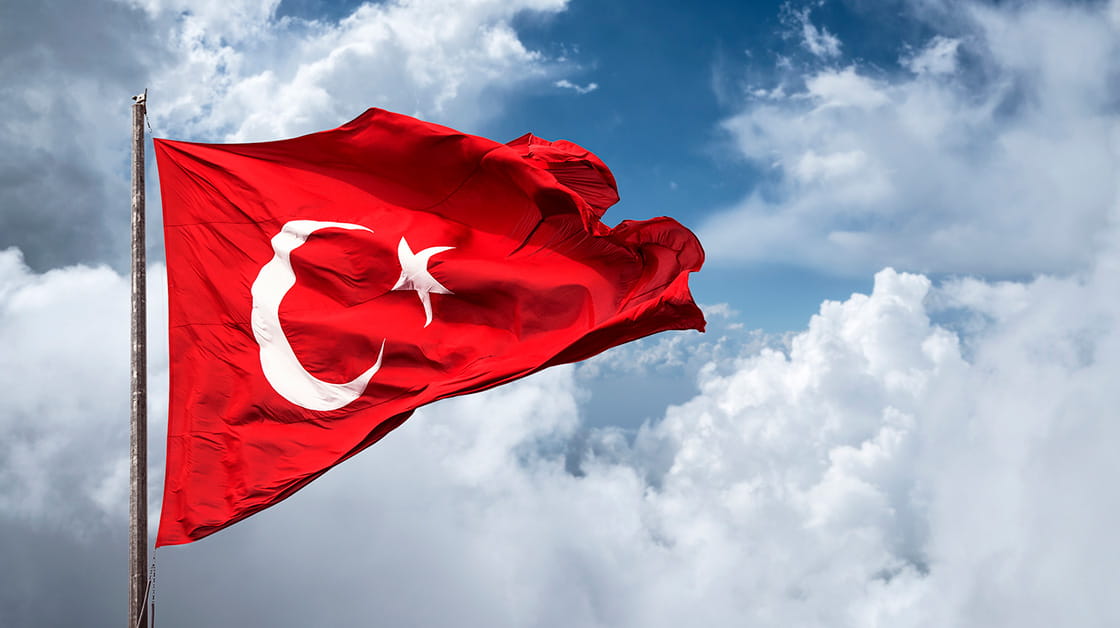 Turkish flag billows in the wind with a blue cloudy sky in the background.