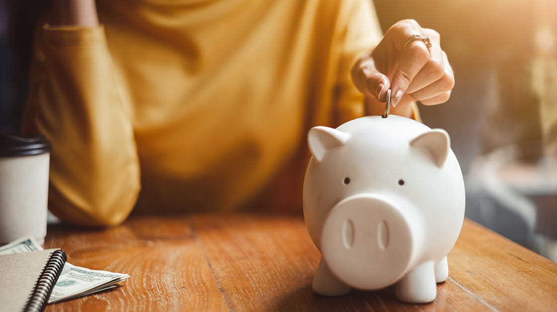 A woman wearing a yellow jumper uses a piggy bank