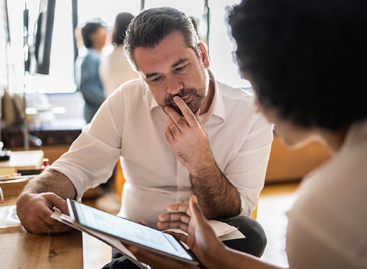 A woman shows a man a tablet in an office setting.